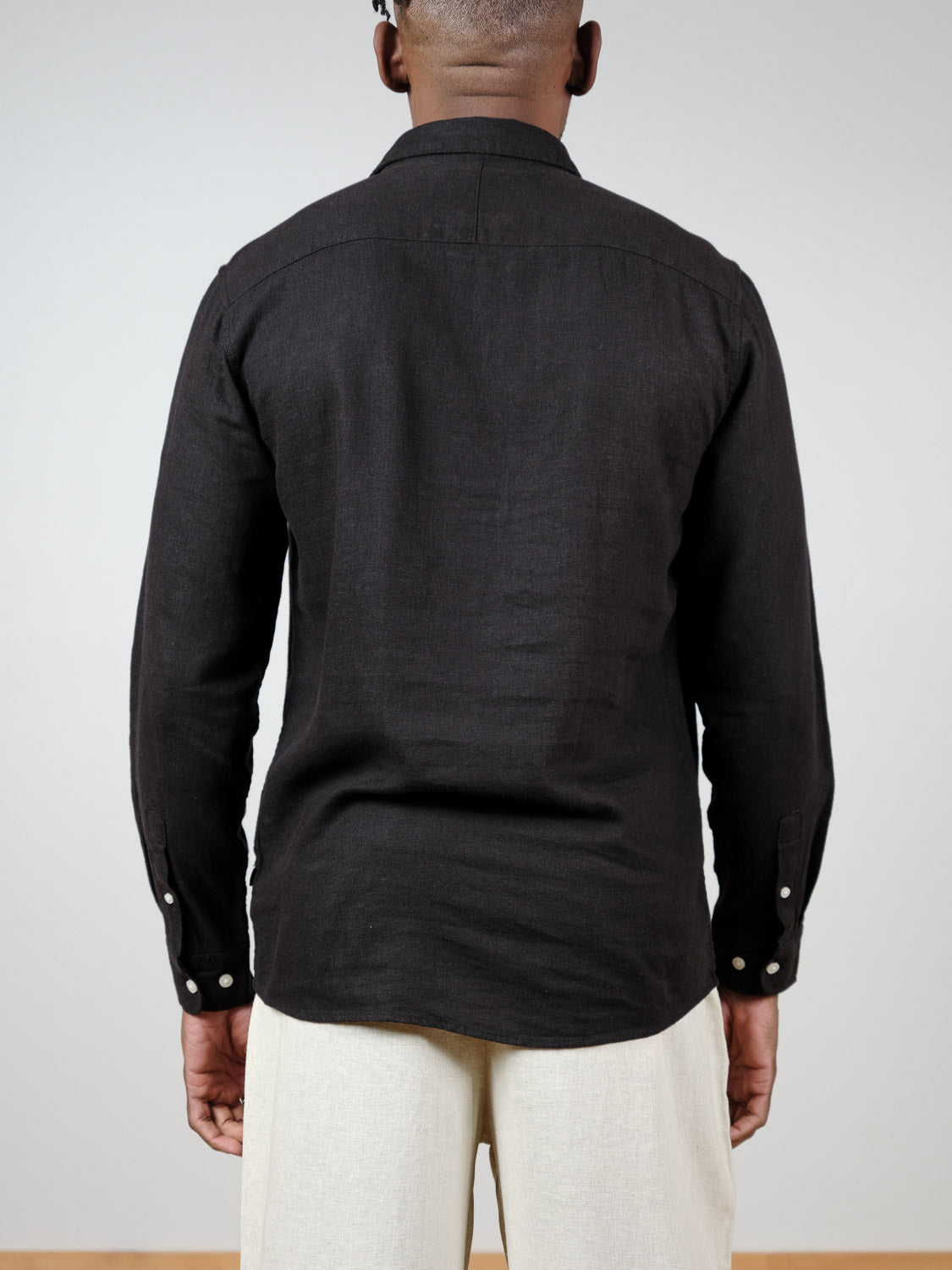 A person faces away from the camera, wearing the !Solid Enea Allan Long Sleeve Shirt in black and light beige pants against a plain light background.