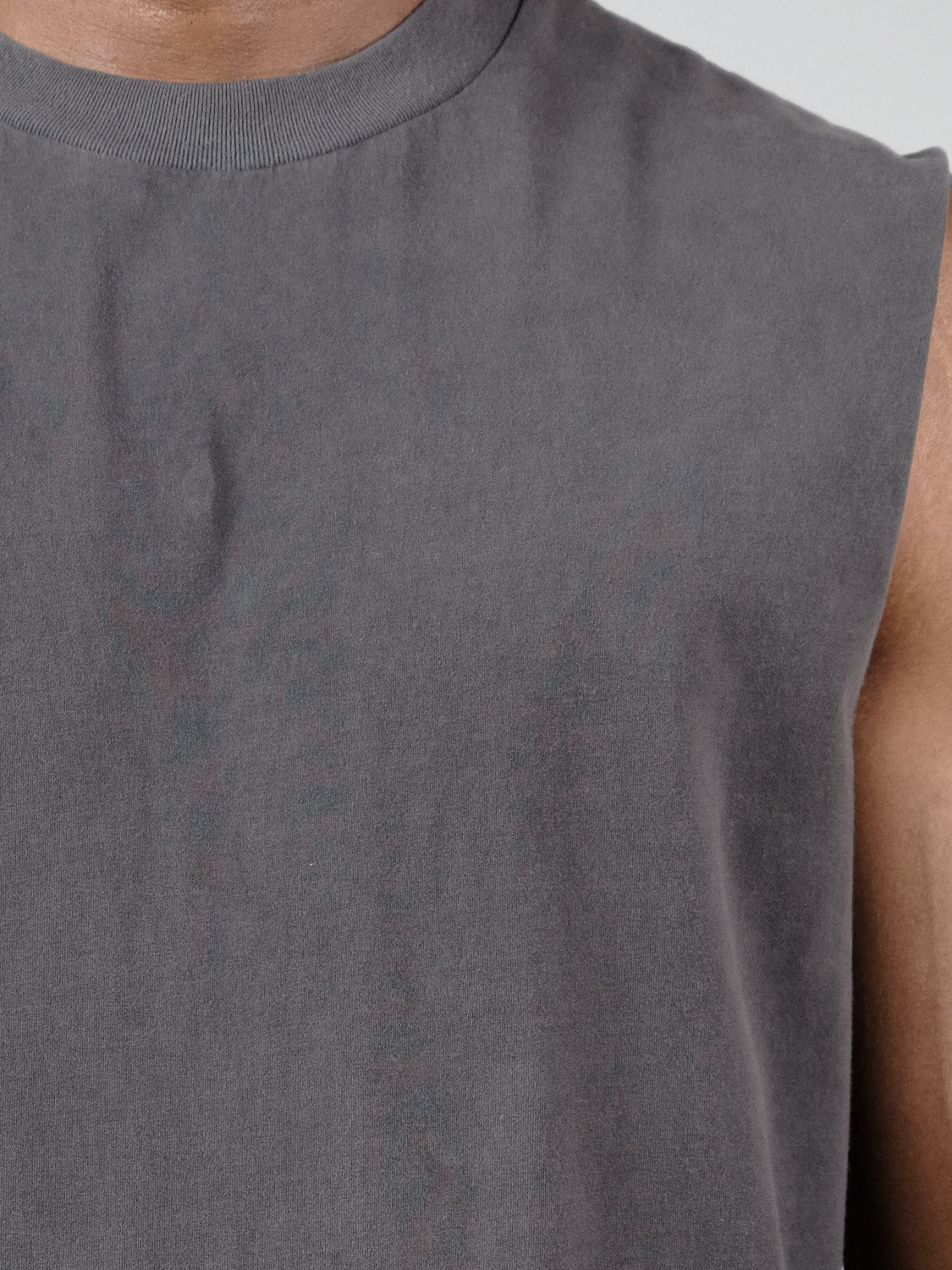 Close-up of a person wearing Industrie’s The Kosta Sleeveless Tee in gray. Only the neck, shoulder, and upper chest are visible. The quick-dry, moisture-wicking fabric contrasts against the plain background.