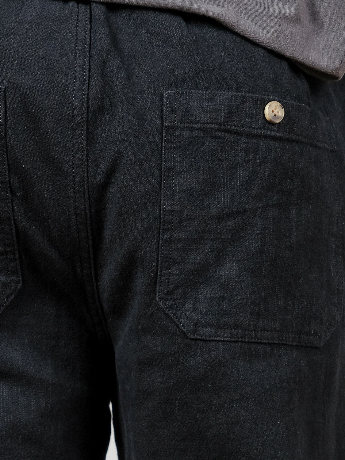 Close-up of the back of a person wearing ID Menswear's Sahara Linen Cotton Pant in black, featuring a relaxed fit and two back pockets, one with a light-colored button. The person pairs it with a dark shirt.