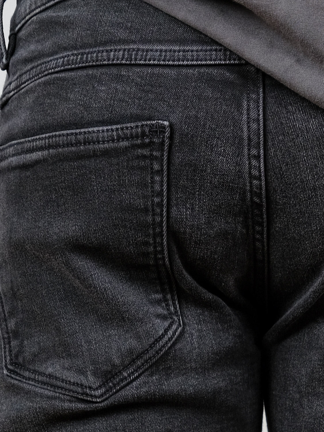 Close-up of the back pocket and upper section of Neuw Lou Straight Cashbah faded black jeans, with part of a gray shirt at the waistband, highlighting the relaxed silhouette.