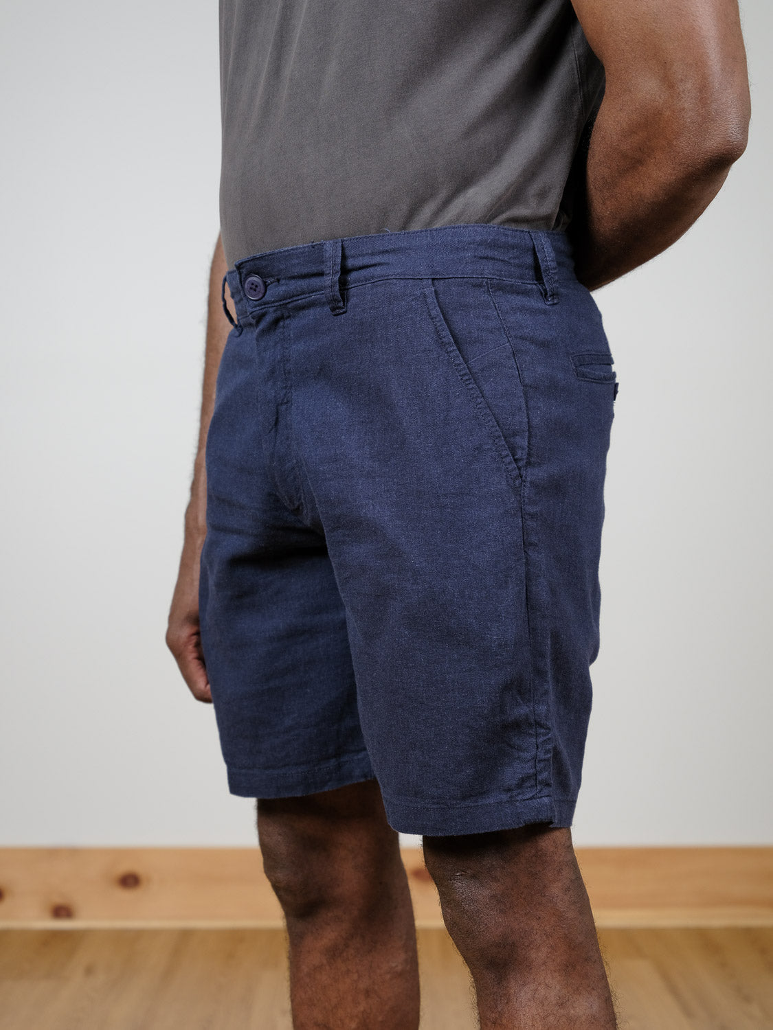 A person stands indoors on a wooden floor wearing a gray t-shirt and navy blue !Solid Aurelius Shorts, arms relaxed at their sides. The photo captures the outfit from mid-torso to knees.