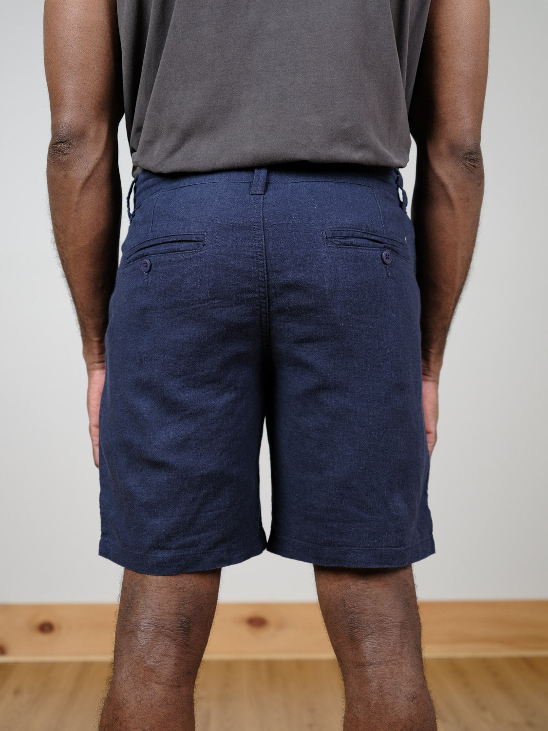 A person faces away from the camera, wearing a dark grey shirt tucked into navy blue !Solid Aurelius Shorts. The regular fit shorts feature two back pockets, set against a light wall and wooden floor.