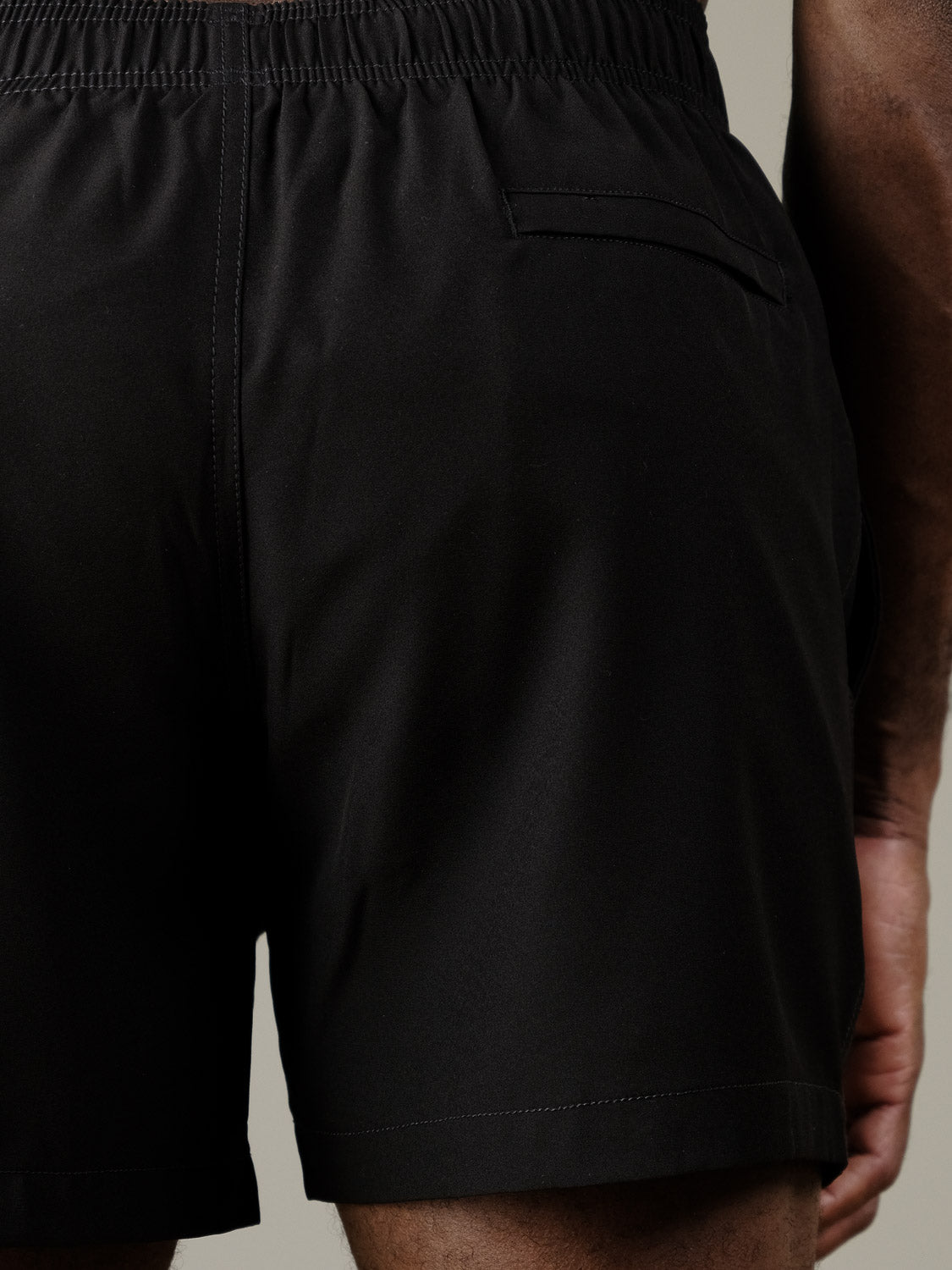 Close-up of the back of a person wearing the Oyogu Quick Dry 4 Way Stretch Swim Trunk from ID Menswear, featuring an elastic waistband and single back pocket. The person's hand is resting by their side.
