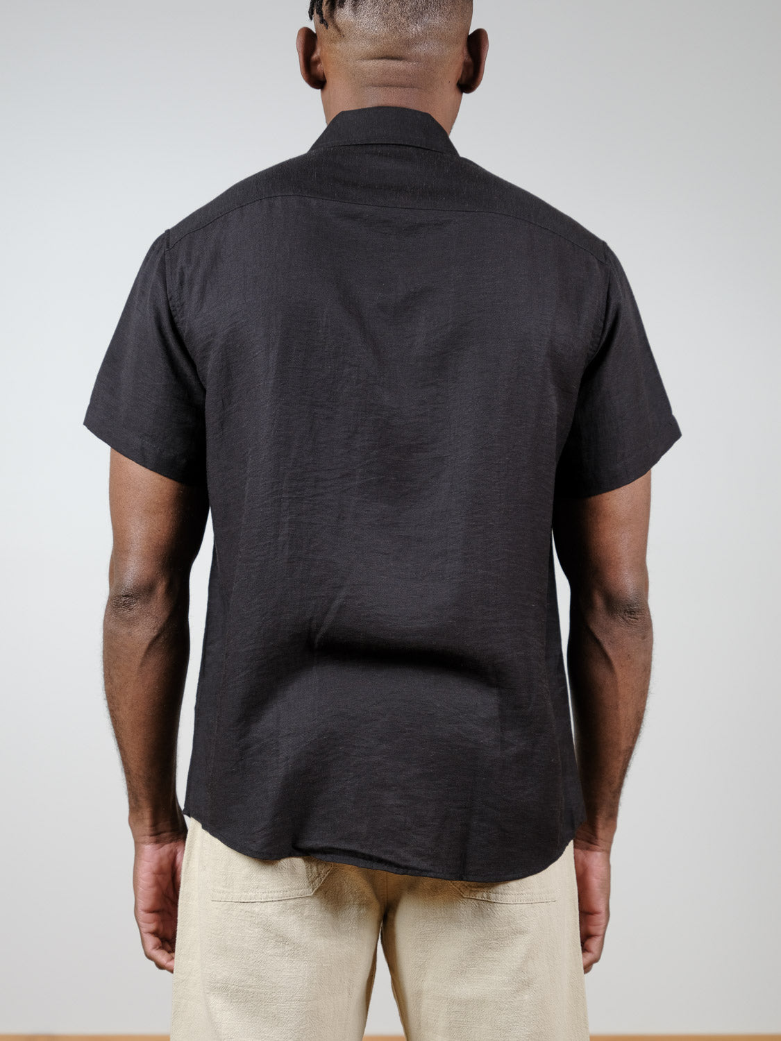 A person is shown from behind wearing the Hiker Short Sleeve Shirt by ID Menswear and light-colored pants, standing against a plain light gray background—a perfect look for summer basics.