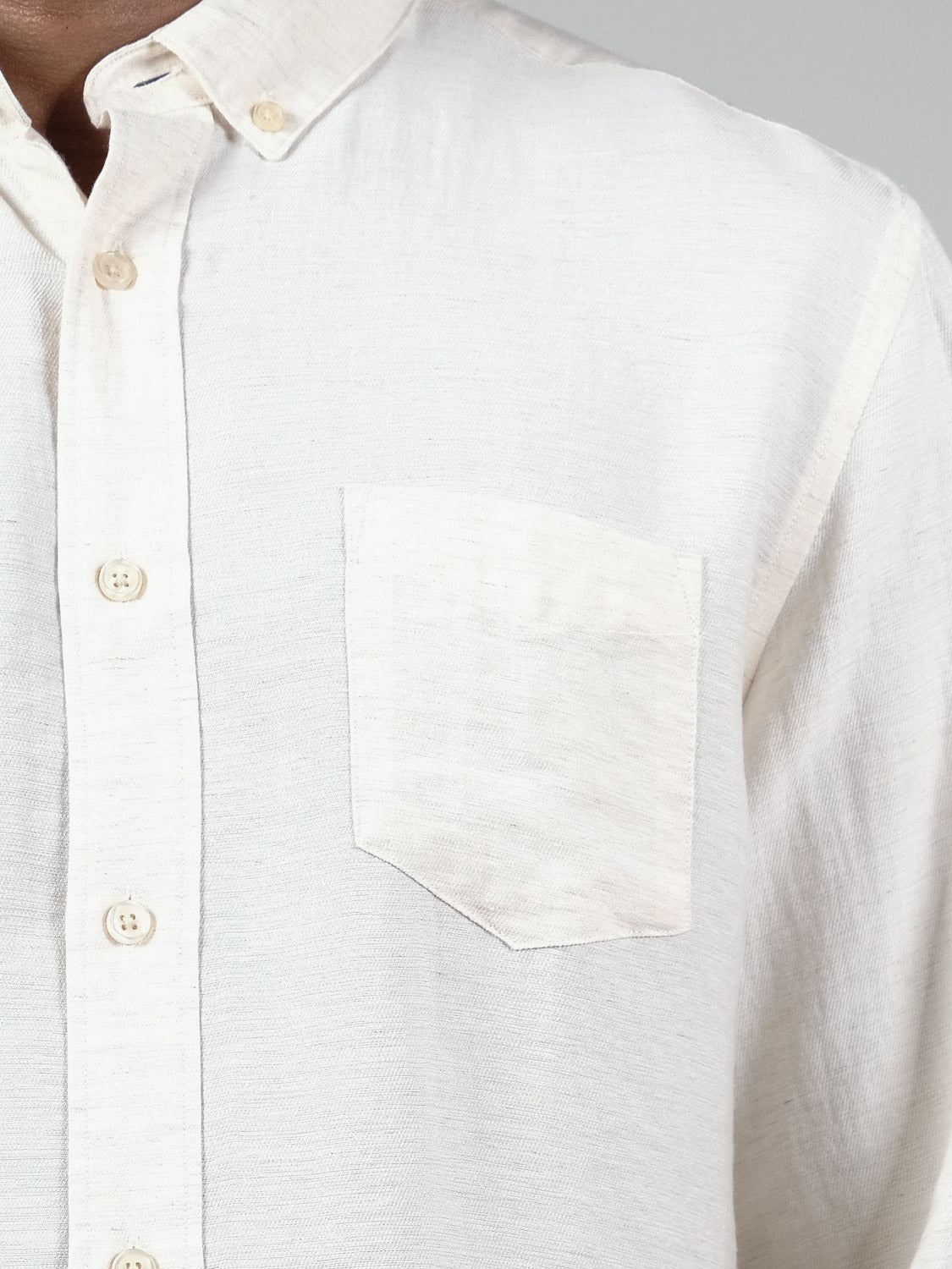 Close-up of a person wearing the ID Menswear Lagos Long Sleeve Shirt in cream, featuring a left front pocket. Made from textured, breathable linen with a relaxed fit for timeless comfort. Only the upper torso is visible.