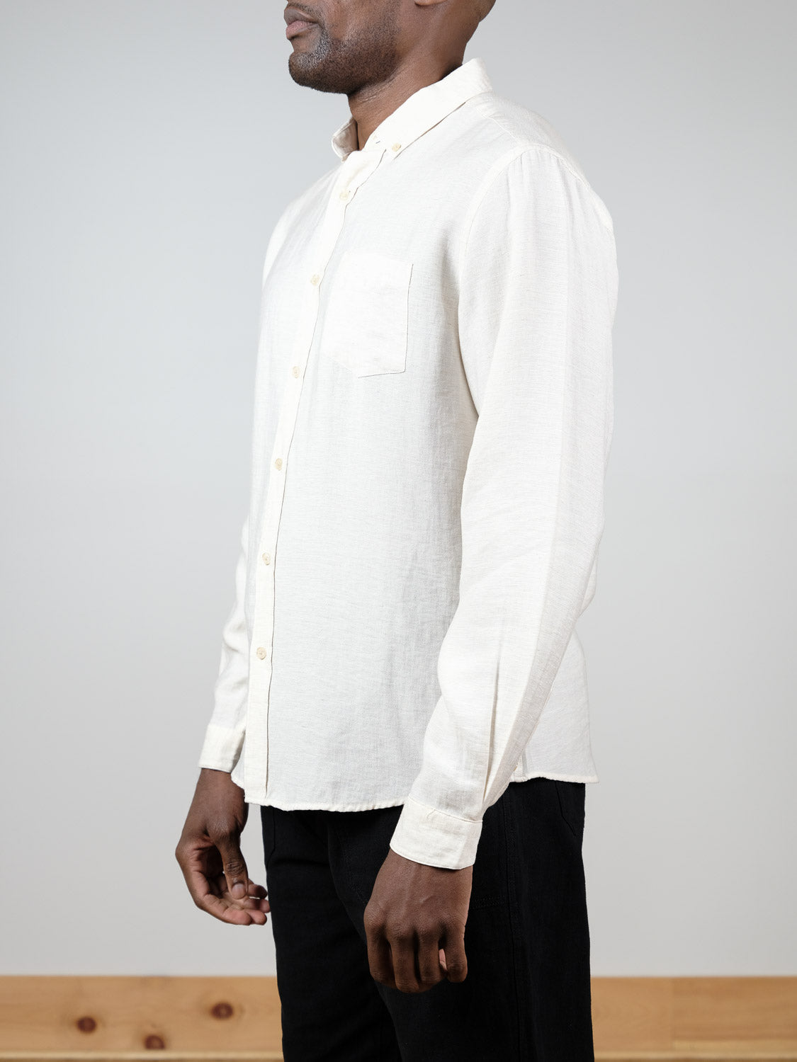A person wearing the ID Menswear Lagos Long Sleeve Shirt in off-white and black pants stands sideways against a plain light background, with only their upper body and part of the legs visible.