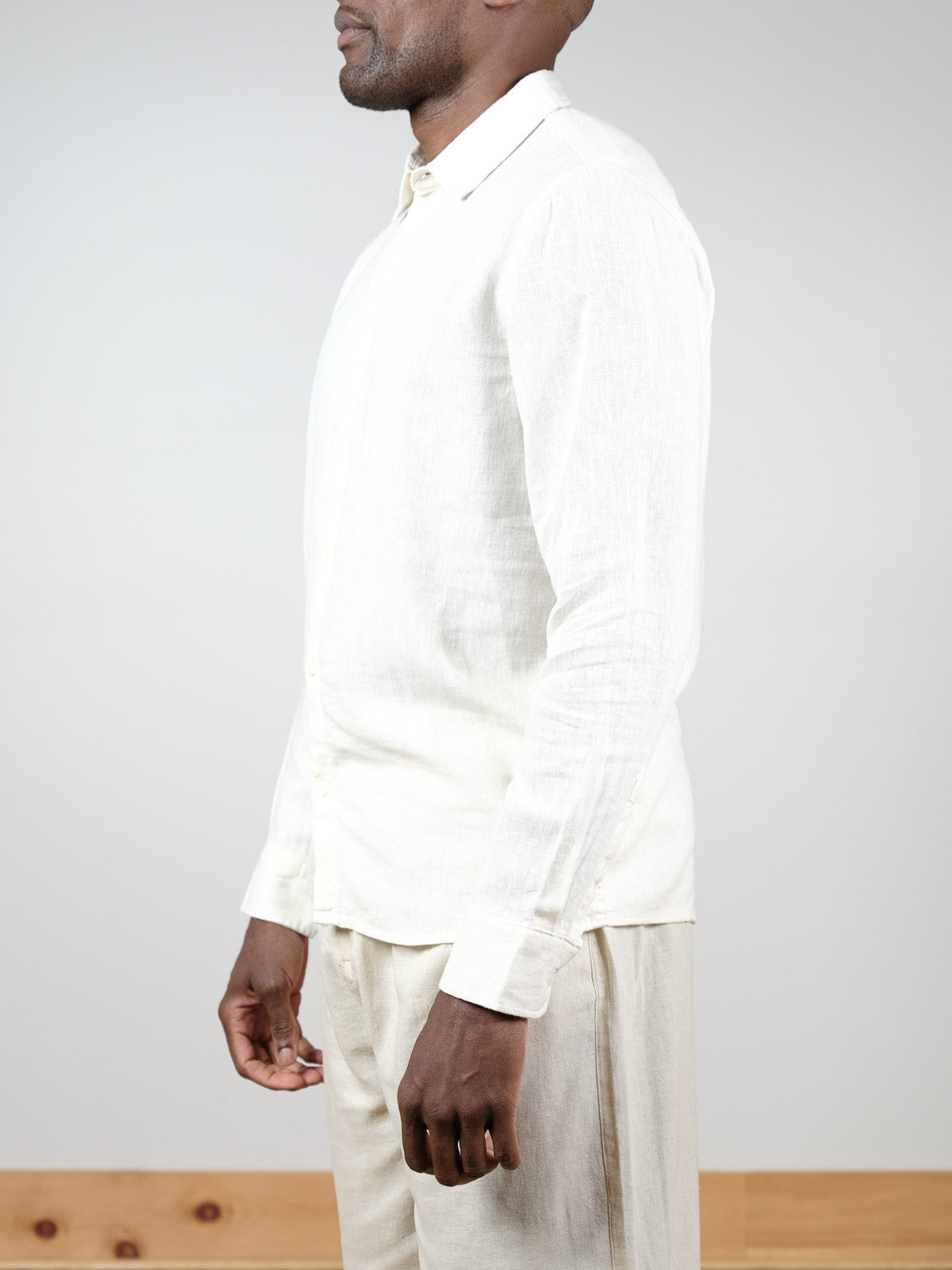 A man in profile stands against a plain background, wearing the Enea Allan Long Sleeve Shirt by !Solid in a light color with matching trousers; his face is partially out of frame.