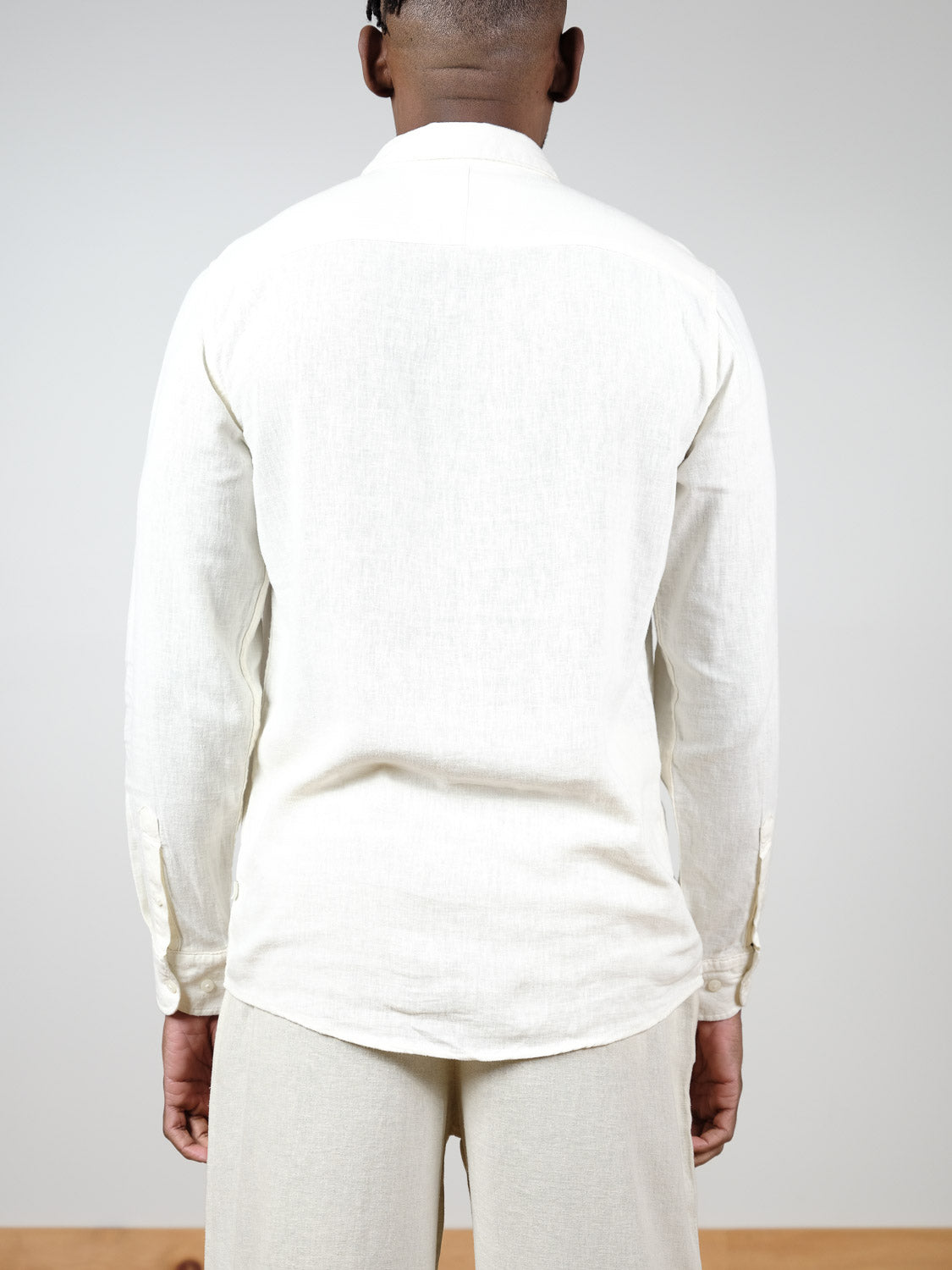 A person faces away from the camera, wearing the Enea Allan Long Sleeve Shirt by !Solid in off-white with light-colored pants, set against a plain background.
