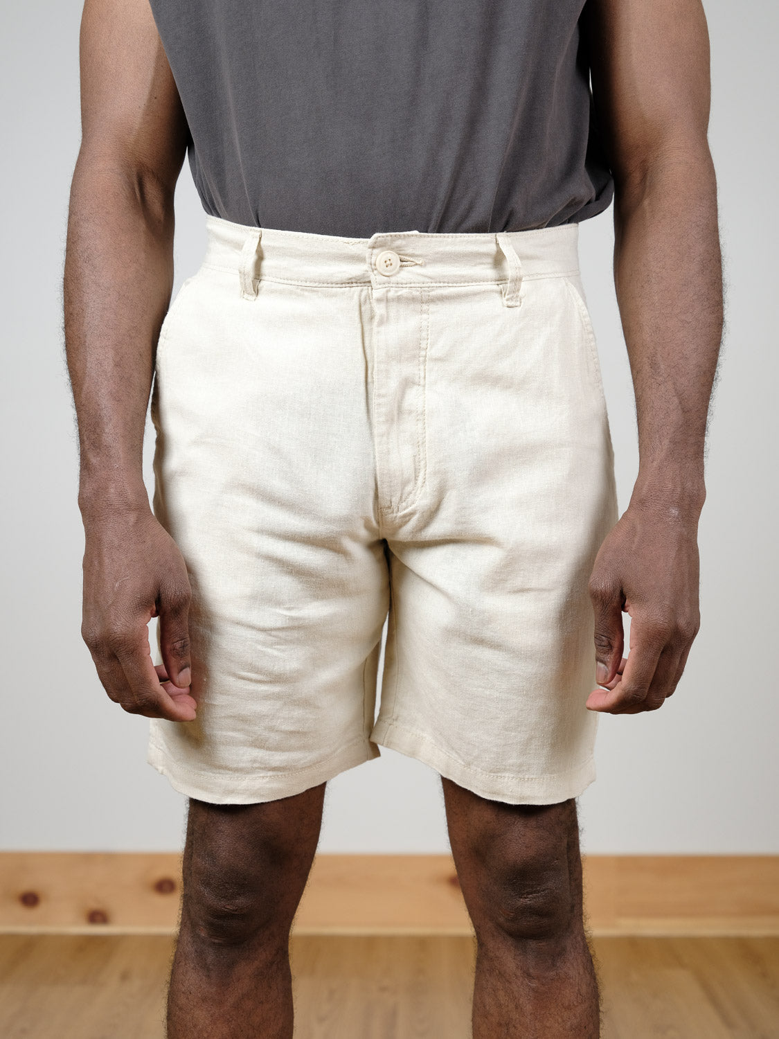 A person stands indoors on a wooden floor wearing the Aurelius Short by !Solid in beige and a dark gray t-shirt, with arms relaxed by their sides. The photo is cropped from shoulders to knees.