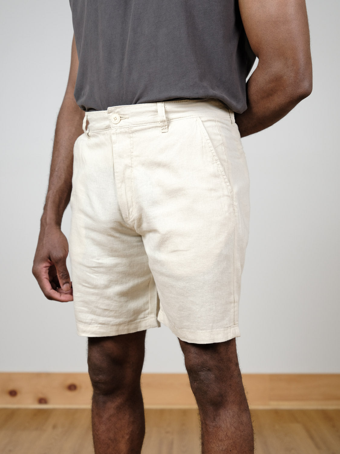 A man stands indoors on a wooden floor, wearing a dark gray T-shirt and light beige !Solid Aurelius Short. His arms are relaxed at his sides, and the image shows him from the shoulders down.