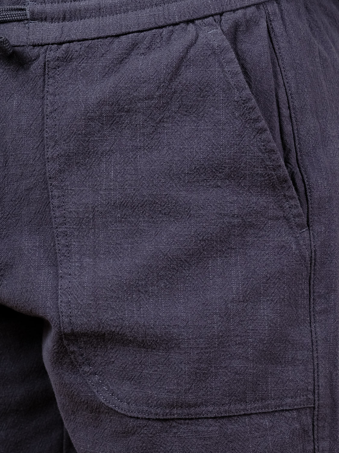 Close-up of a person wearing ID Menswear's Phi Phi Linen Blend Drawstring Short, featuring textured dark gray fabric, a visible side pocket, and an elastic waistband.