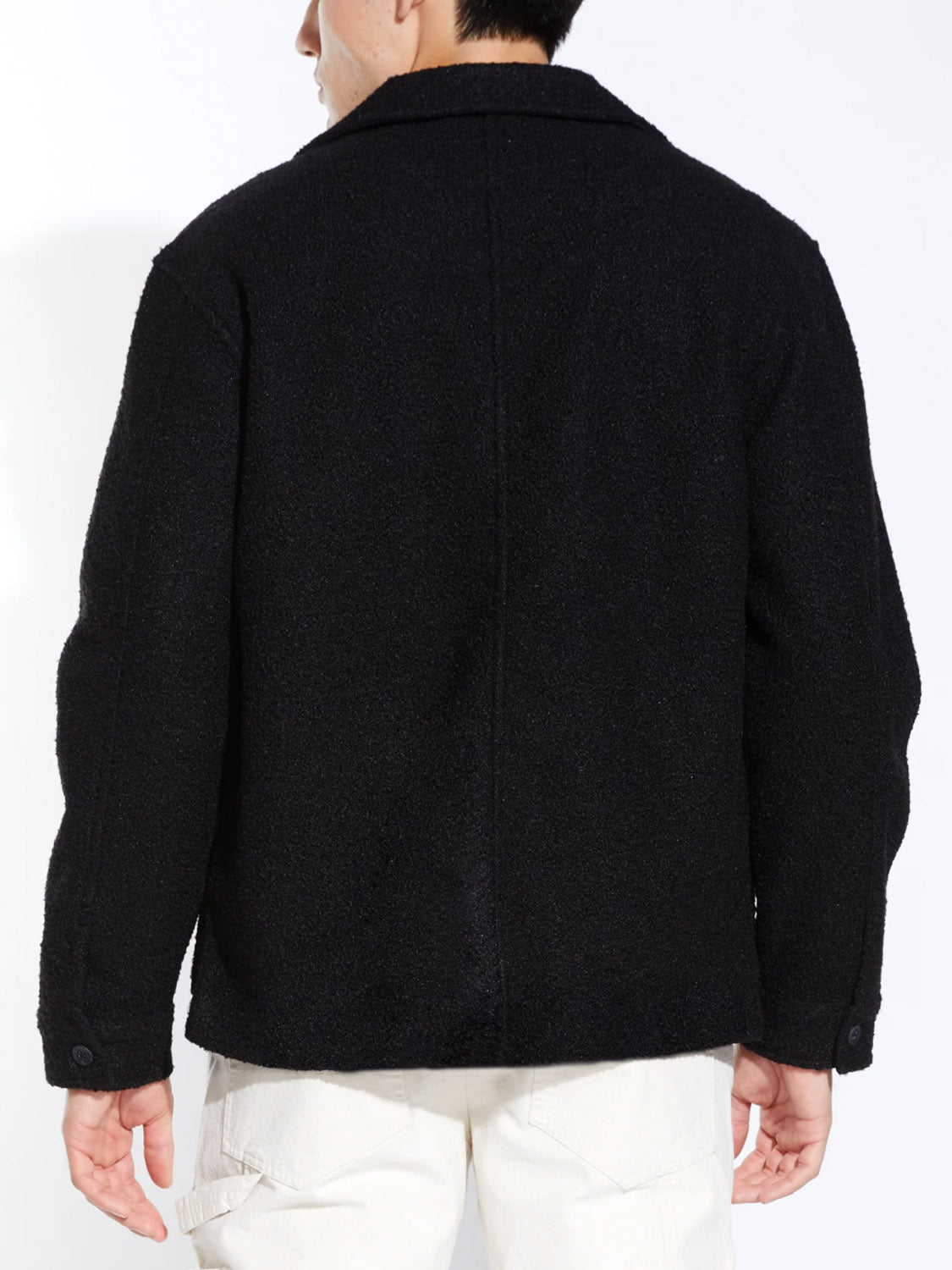 A person, facing away from the camera, wears the Civil Society Abbott Relaxed Fit Walking Coat in black with off-white pants, standing against a plain light background.