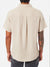 A man faces away, wearing the Katin Alan Solid Shirt in light beige. This short-sleeve button-up by Katin features a relaxed fit and versatile style. His tattoo sleeve is visible against a plain white background.