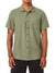 A person wears the Katin Alan Solid Shirt by Katin, a short-sleeve light green button-up with a chest pocket and black pants. Relaxed arms reveal tattoos, highlighting this wardrobe essential against a plain white background.