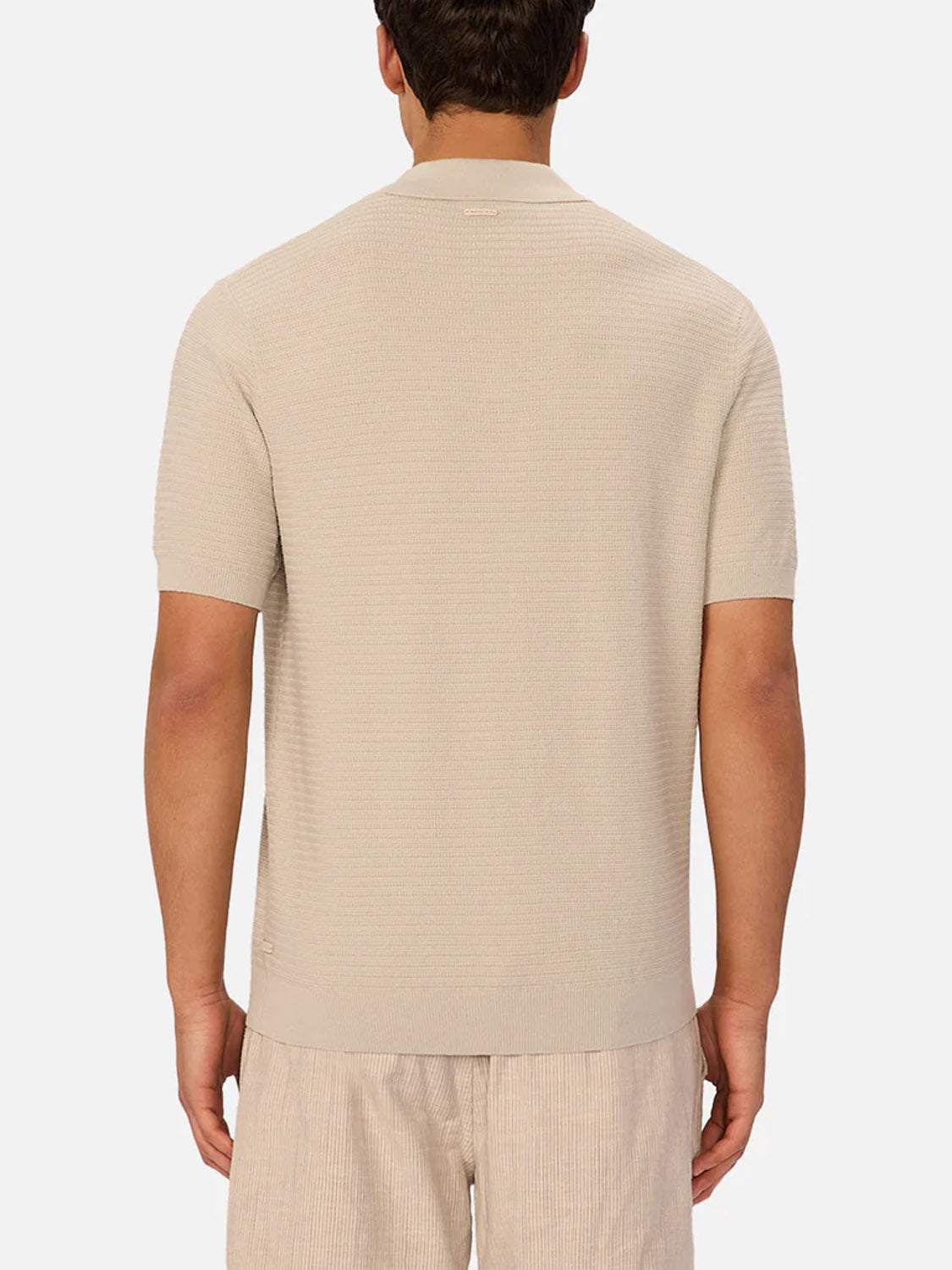 A man is shown from the back wearing The Alicante Polo by Industrie in light beige, paired with beige pinstriped shorts, standing against a plain white background.