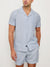 A man wears the Rails Amalfi Seersucker Shirt, featuring light blue and white stripes, with matching shorts. He stands with one hand in his pocket against a plain off-white background.