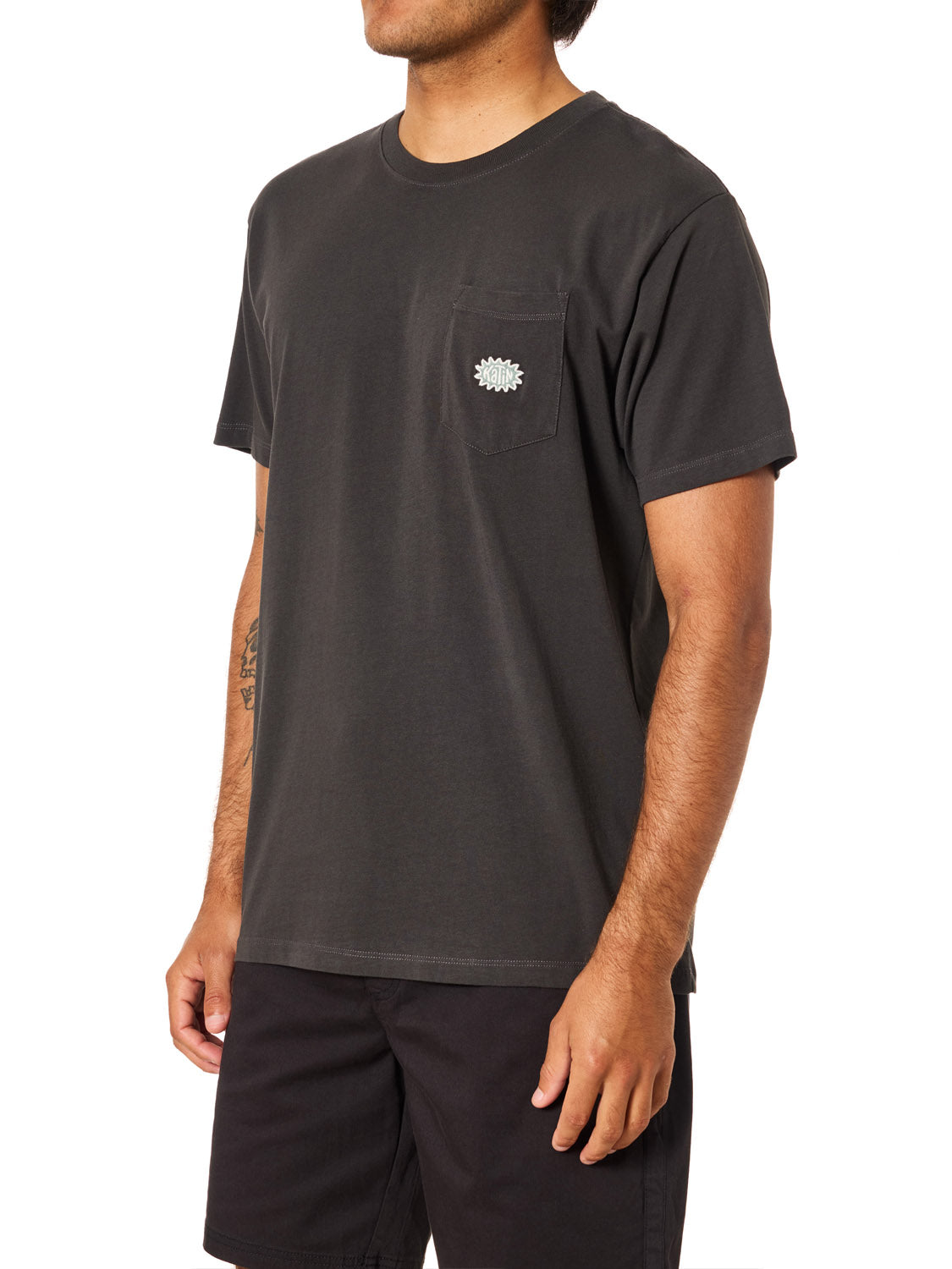 A person wears the Katin Amoeba Pocket Tee by Katin, featuring organic cotton and a small chest pocket graphic, paired with black shorts. They stand against a white background with their face not visible.
