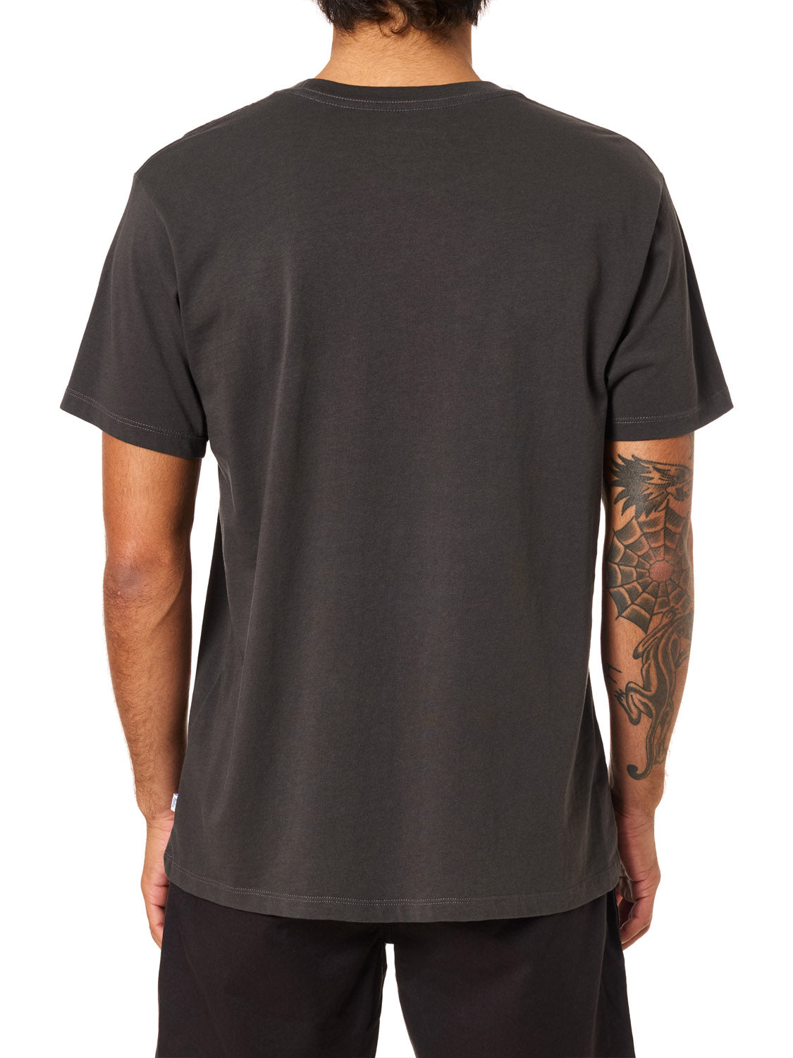 A person with short dark hair is shown from the back, wearing a plain black Katin Amoeba Pocket Tee and black pants. A detailed dragon tattoo is visible on their right arm against a white background.