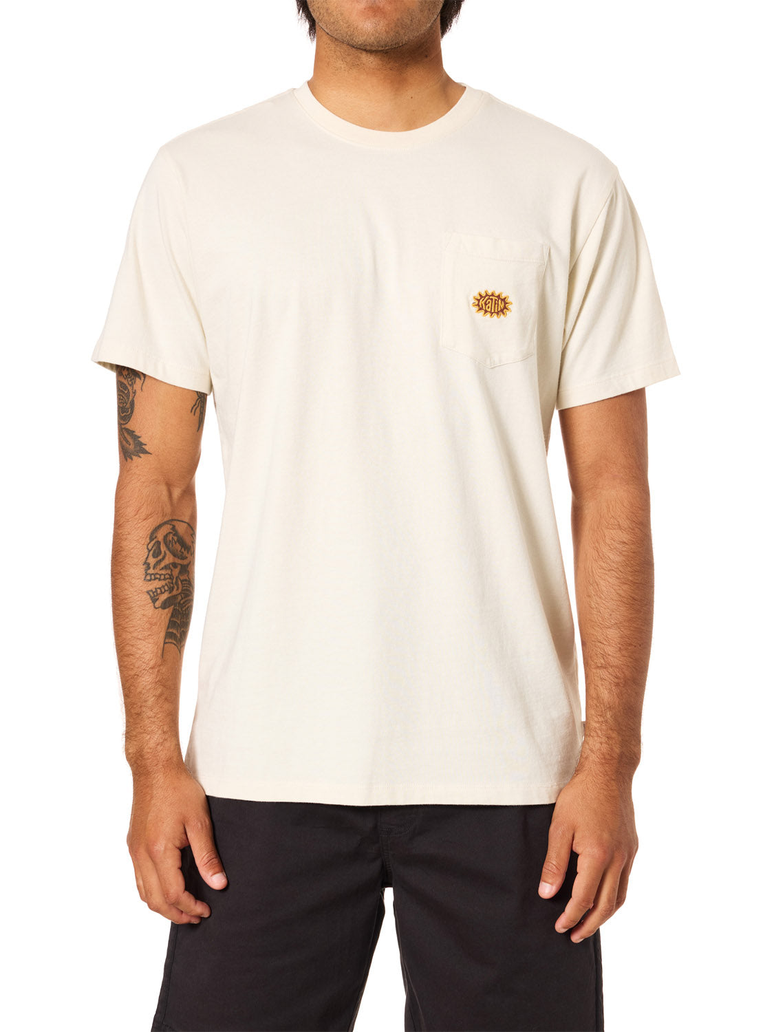 A person with tattoos on both arms wears the Katin Amoeba Pocket Tee by Katin—made from soft organic cotton with a small chest pocket—paired with black shorts, standing against a white background.