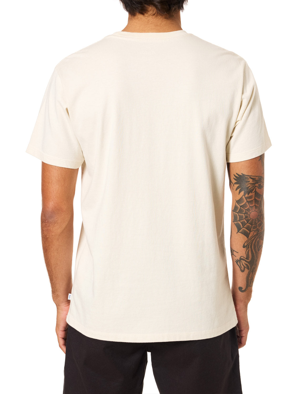 A person with a dragon tattoo on their right arm, seen from behind, wears an off-white Katin Amoeba Pocket Tee made from organic cotton and black pants.