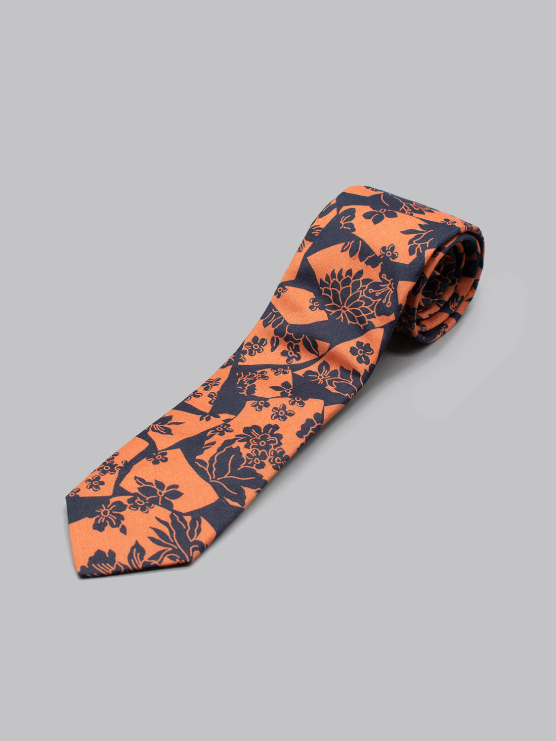A rolled-up Liberty of London Tana Lawn™ Ancient Tie by ID Menswear, handmade in Brooklyn from soft cotton with a dark blue floral pattern, is displayed on a plain light gray background.