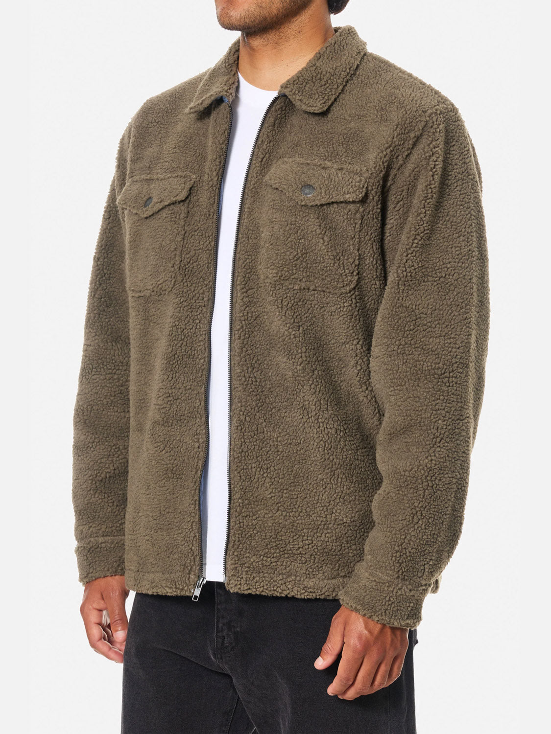 A person wears the Katin Anderson Sherpa Jacket in olive green polyester over a white t-shirt with black pants. The jacket features two chest pockets with flaps and buttons. The background is plain white.
