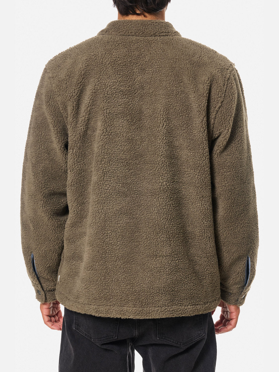 Seen from behind, a person wears the Katin Anderson Sherpa Jacket in olive-green. The plush polyester sherpa and long sleeves offer a vintage-inspired look, perfectly complemented by black pants.