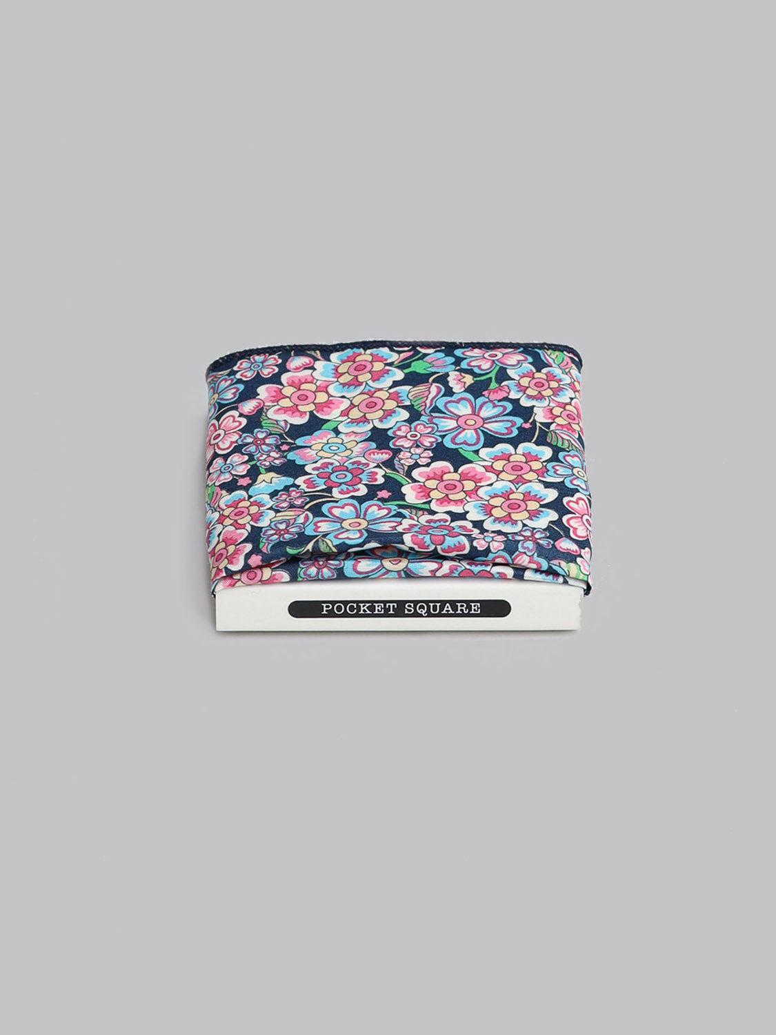The Liberty™ Anokhi Pocket Square by ID Menswear is handmade in Brooklyn from Tana Lawn cotton with a pink, blue, and yellow floral design on dark fabric. It comes folded in white “Pocket Square” packaging on a light gray background.