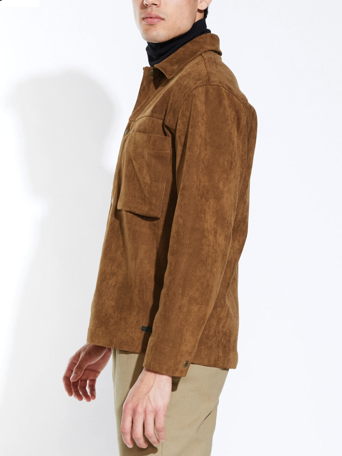 A person models the Civil Society Ansel Boxy Fit Suede Shirt Jacket over a black turtleneck and beige pants, standing sideways against a plain white background with one hand at their side.