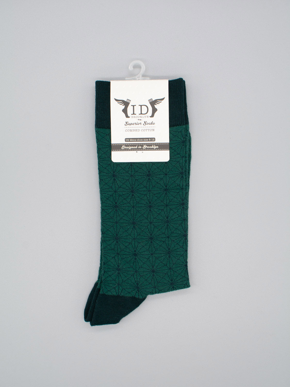 A pair of dark green Asano Graphic Socks by ID Menswear, featuring a geometric pattern and made from soft combed cotton, is neatly folded with a white ID Superior Socks tag, hung on a white hook against a light gray background. Fits men’s shoe size 8-12.