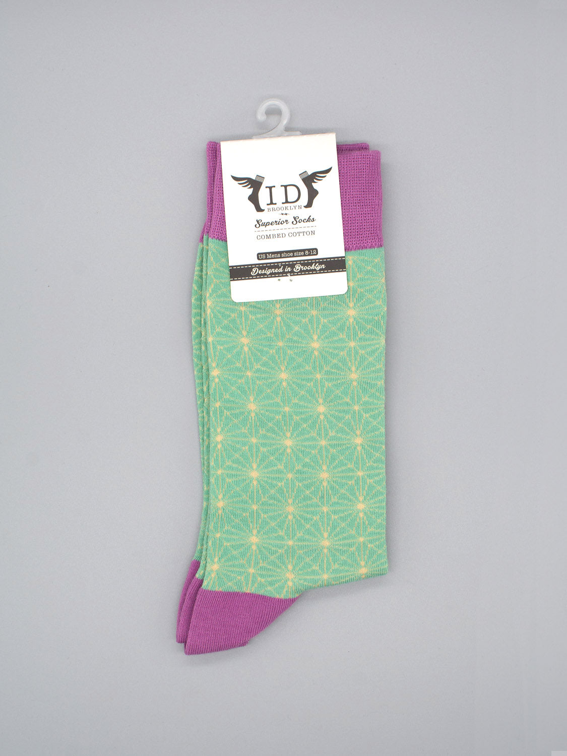 The Asano Graphic Socks by ID Menswear feature a green body with a yellow geometric pattern, purple cuffs, heels, and toes. Made of soft combed cotton to fit men’s shoe size 8-12. Displayed on gray with a white ID Menswear label attached.