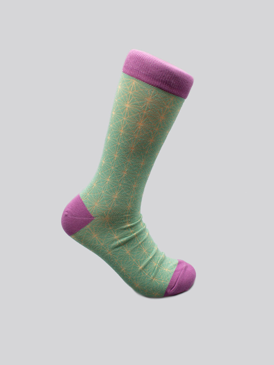 The Asano Graphic Sock by ID Menswear is shown in light green combed cotton with a yellow geometric pattern and purple cuff, heel, and toe, against a gray background; fits men’s shoe size 8-12.