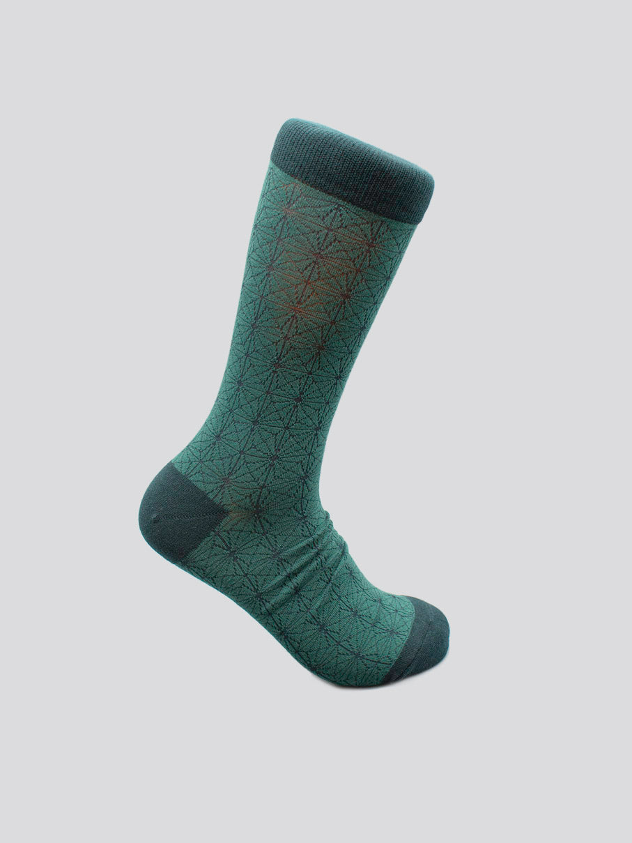 The Asano Graphic Sock by ID Menswear features a green geometric black pattern with dark green heel, toe, and cuff. Made from soft combed cotton for men’s shoe sizes 8-12, shown on a plain light gray background.
