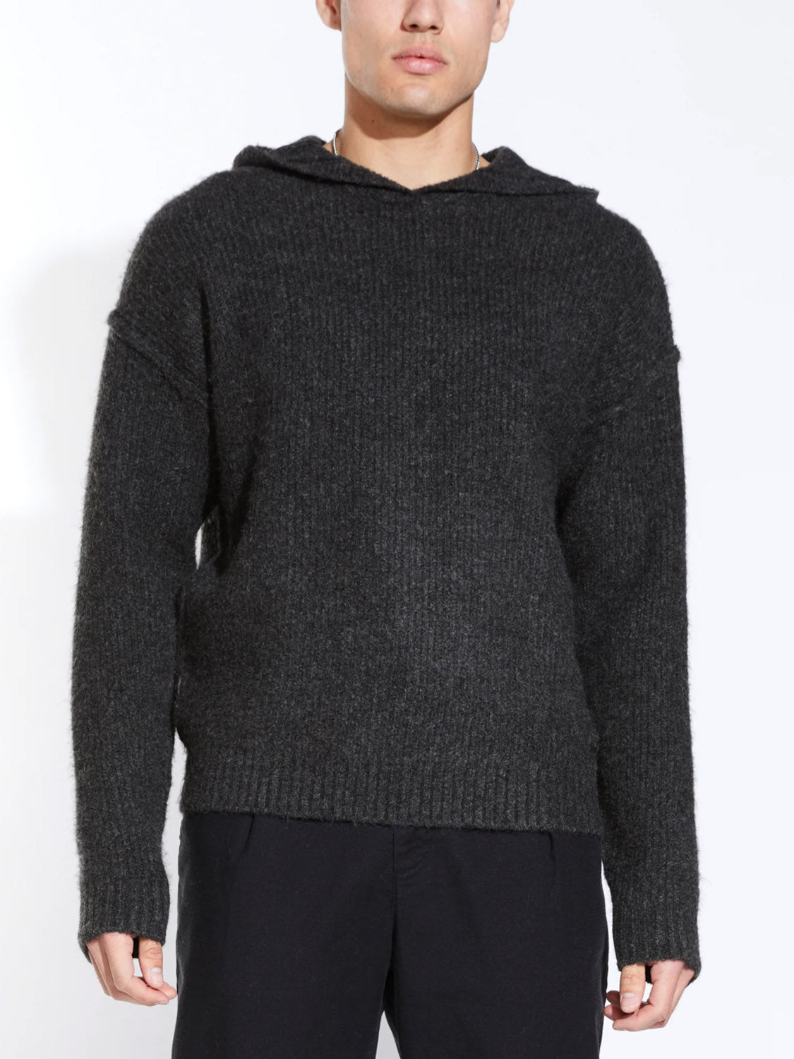 A person wears the Civil Society Avery Oversized Sweater Hoodie in dark gray, featuring a textured knit, long sleeves, and relaxed fit, paired with black pants against a plain white background.