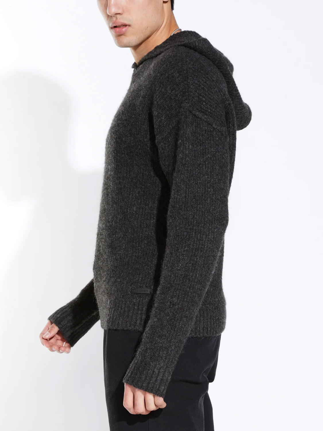 A person stands sideways against a white background, wearing the Civil Society Avery Oversized Sweater Hoodie in dark gray with black pants.