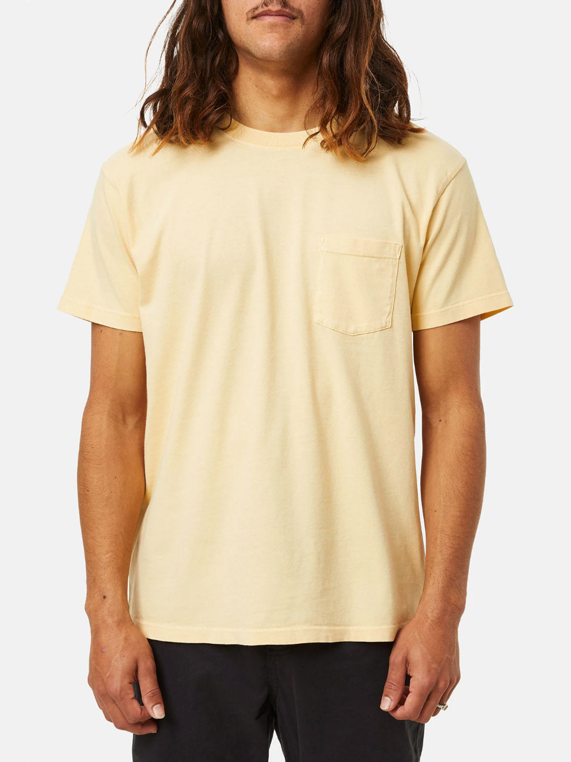 A person with long hair dons a light yellow Katin Base Tee, crafted from organic cotton, featuring a small left-side pocket against a plain white background.
