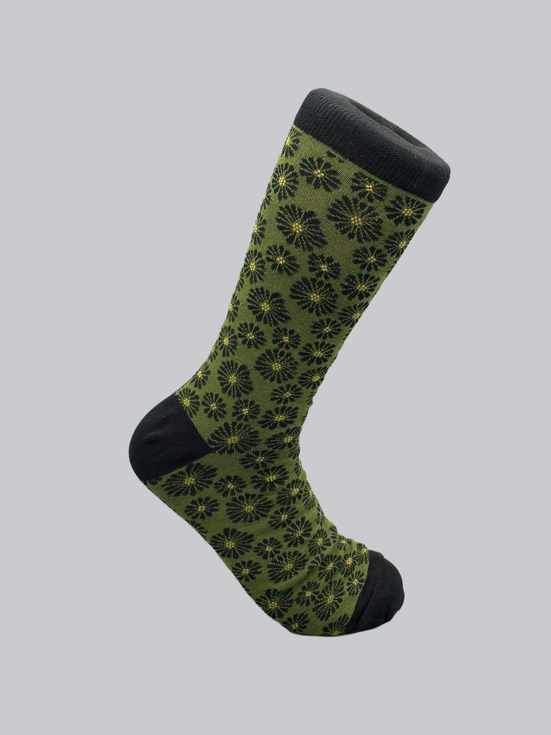 The Beckia Graphic Sock by ID Menswear is a single green sock with black toe, heel, and cuff adorned with a pattern of black and yellow flowers. Made from high-quality combed cotton, it is showcased against a plain gray background.