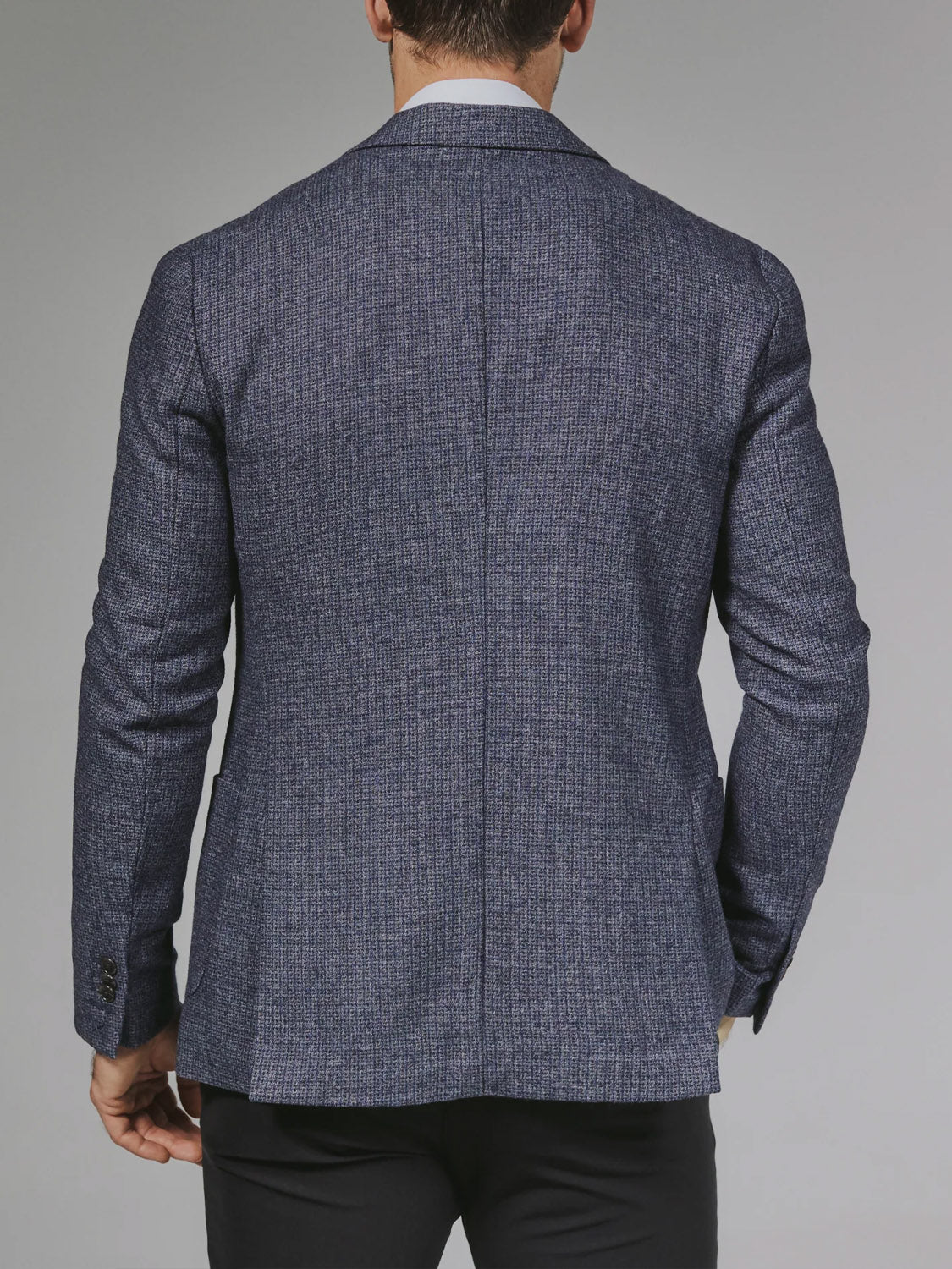 A man is shown from behind wearing the 7 Diamonds Belfast Blazer in textured dark blue with black pants, set against a plain gray background.