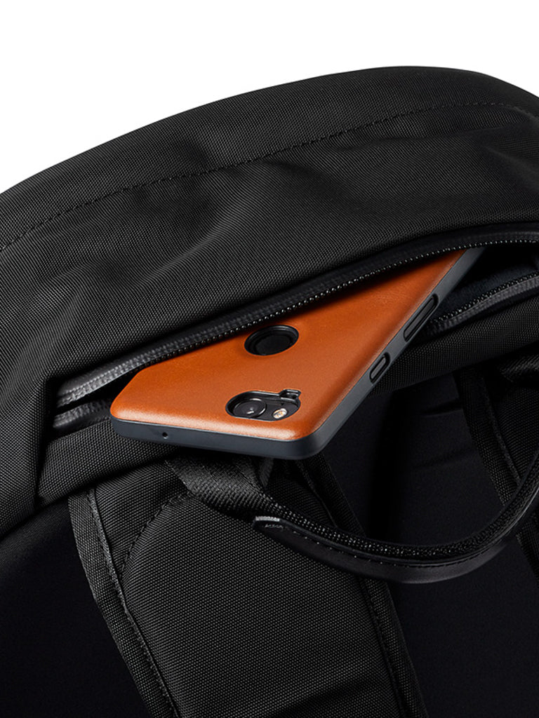 A close-up of the Bellroy Classic Backpack - 20L shows a brown smartphone partially tucked into its open zippered pocket.