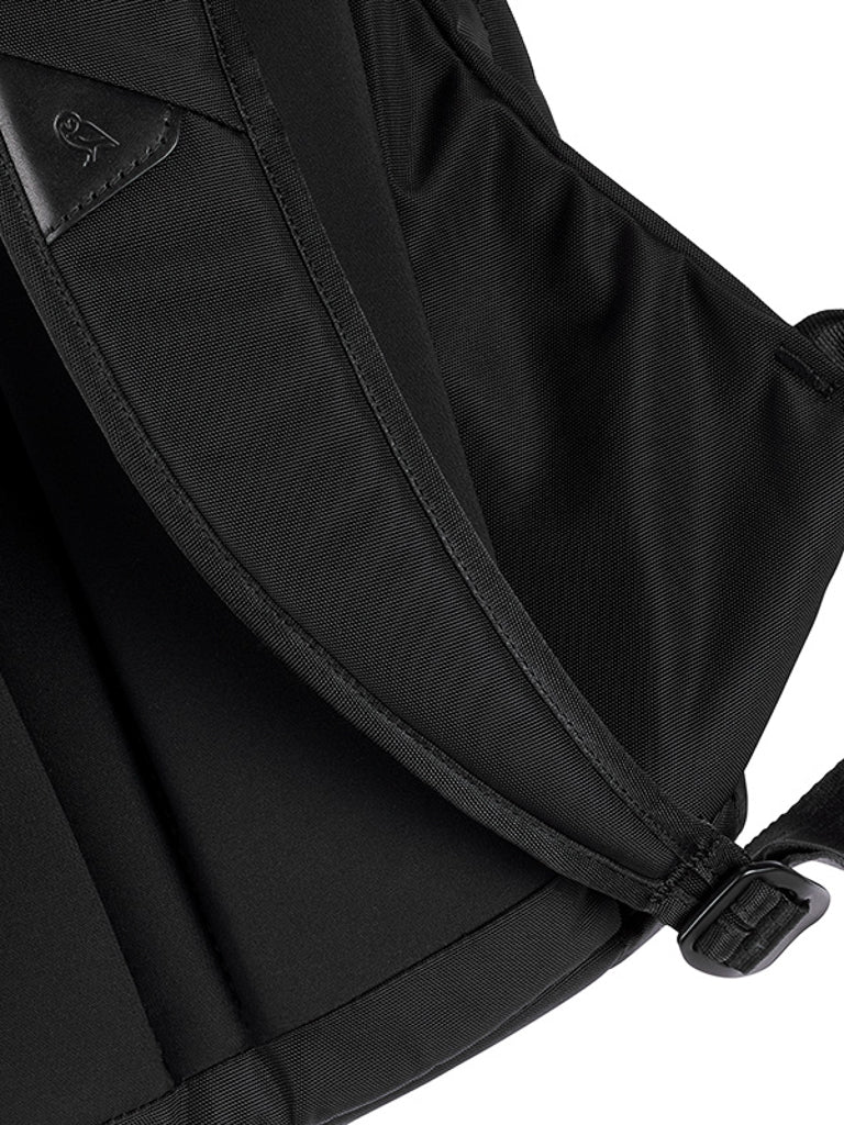 Close-up of the Bellroy Classic Backpack - 20L, showing a padded shoulder strap, sturdy seam, and metal adjustment buckle. The textured, water-resistant fabric features a stitched logo—ideal as a durable laptop bag.