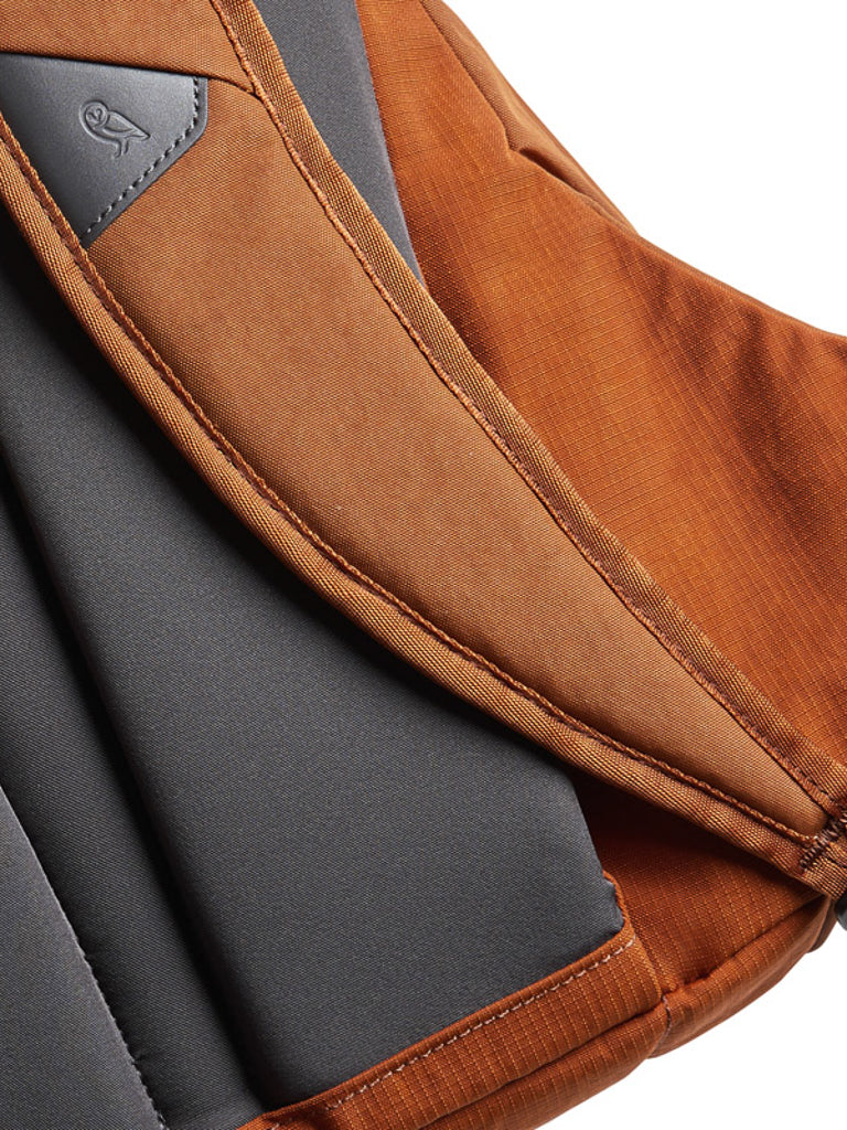 Close-up of Bellroy's Classic Backpack - 20L in brown and gray, crafted from recycled materials, with a padded back panel and a stitched logo on a leather patch near the top.