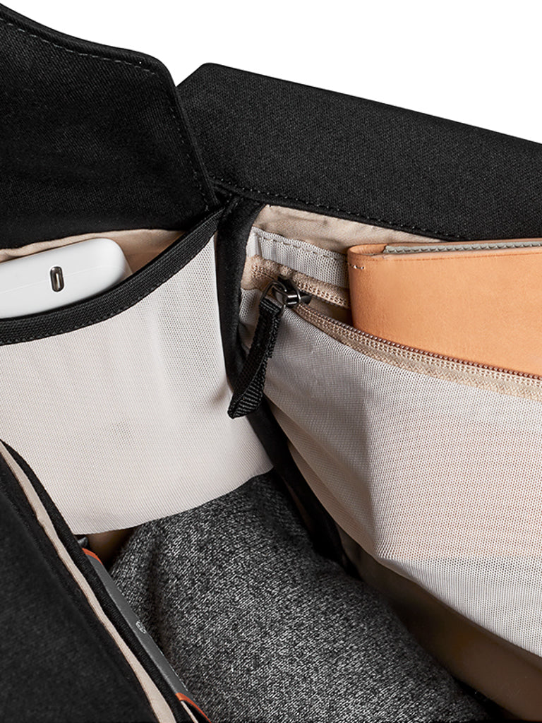 Close-up of the Bellroy Melbourne Backpack Compact - 13L showing an organized interior with a phone in a mesh pocket, a tan wallet in a zippered compartment, and grey fabric at the bottom.