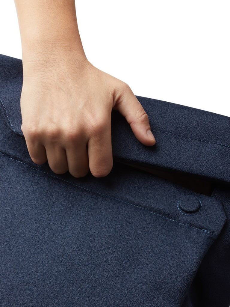 A close-up of a hand reaching into the back pocket of textured navy blue pants, with a visible button—an ideal style for carrying essentials or pairing with the Bellroy Melbourne Backpack Compact - 13L for an urban professional look.