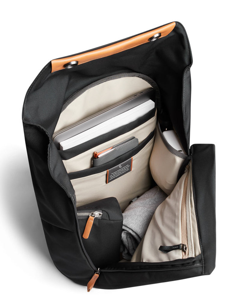 The Bellroy Melbourne Backpack - 18L in black features a tan interior with organized compartments for a laptop, tablet, notebook, gray pouch, zip pocket, and a rolled-up gray garment.