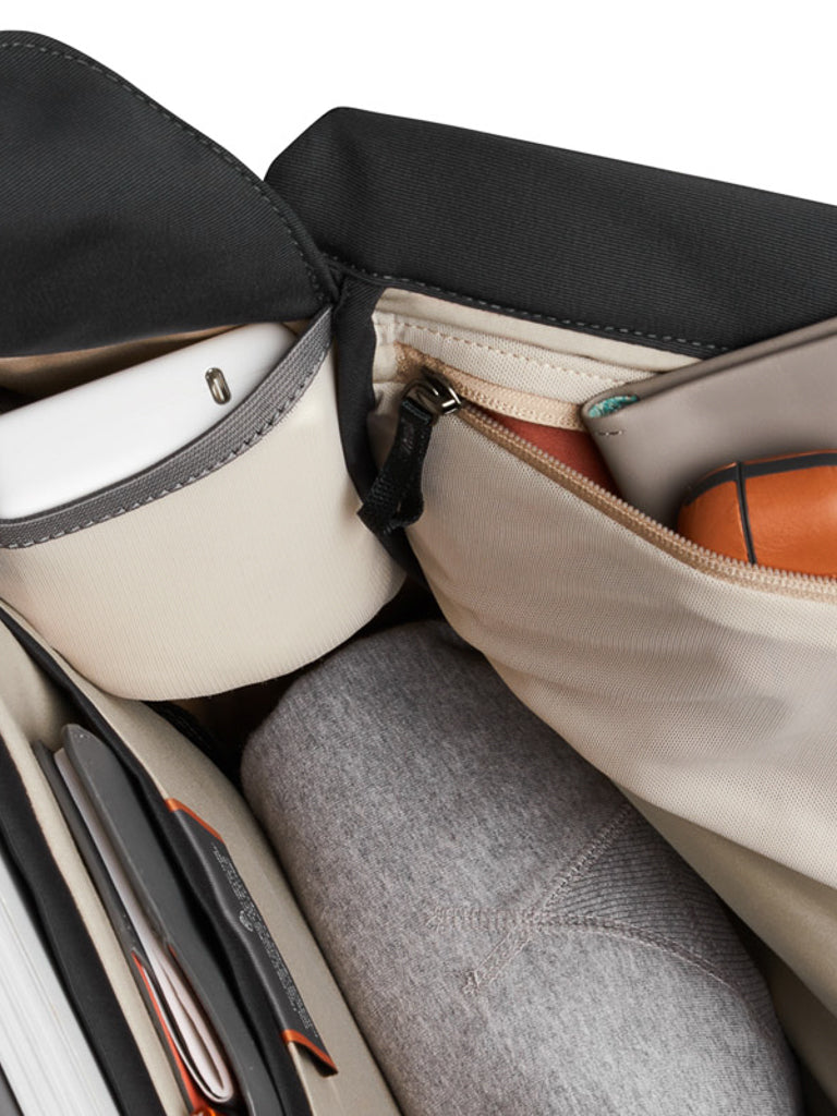 Close-up of the Melbourne Backpack - 18L by Bellroy, showing a grey rolled-up clothing item, tablet, notebook, orange wireless mouse, and other small belongings neatly organized in its slim urban interior.