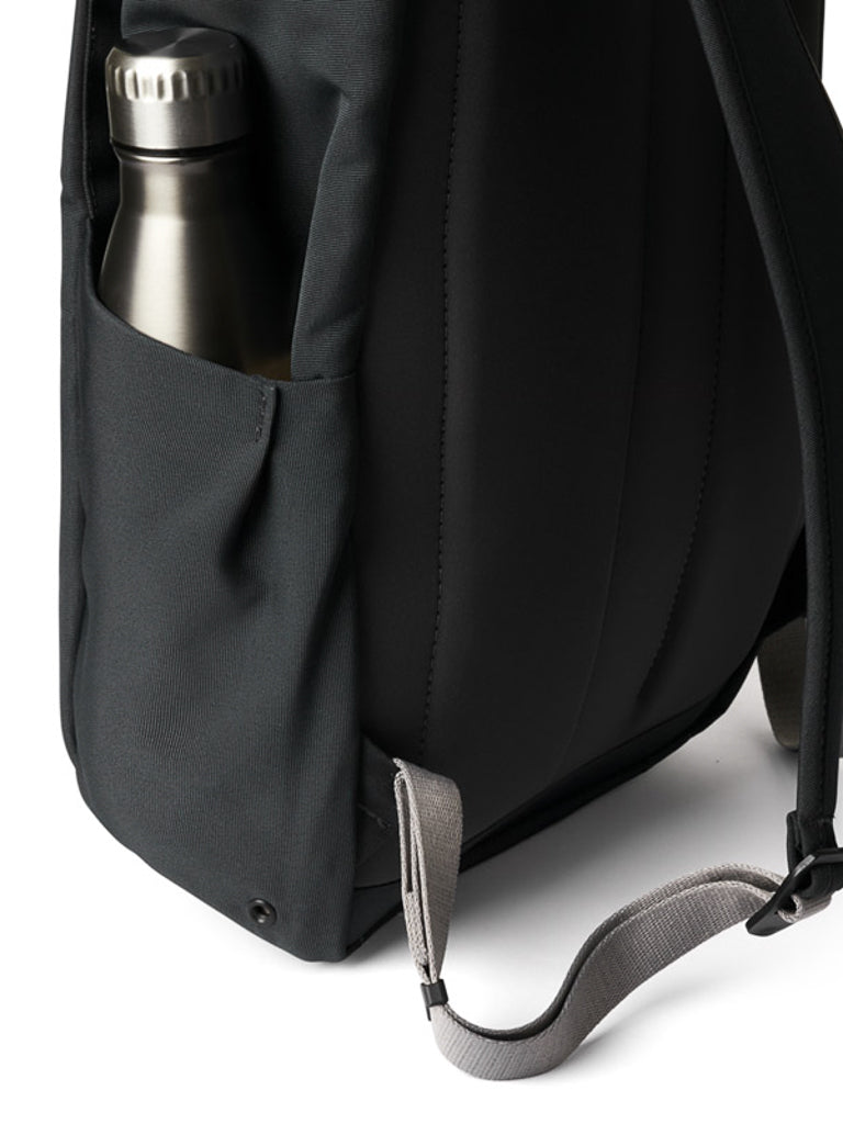 A close-up of the Bellroy Melbourne Backpack - 18L in black with a gray strap, featuring a metal water bottle partially tucked into its side pocket.