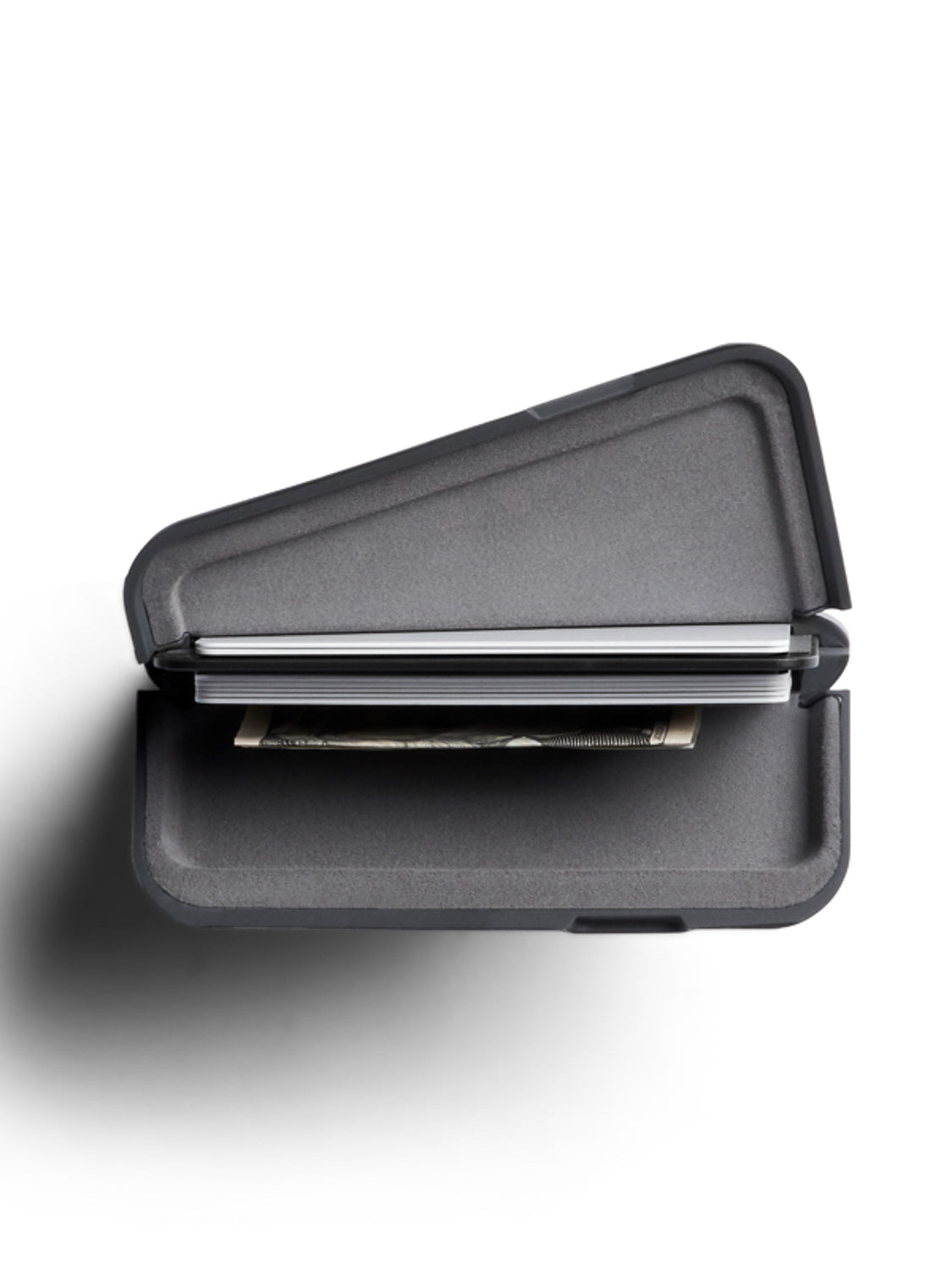 The Bellroy Flip Case Wallet, a slim hard-shell double-sided wallet in dark gray eco-tanned leather, is partially open to reveal a bill and cards inside. It rests on a white surface, casting a soft shadow to the left.