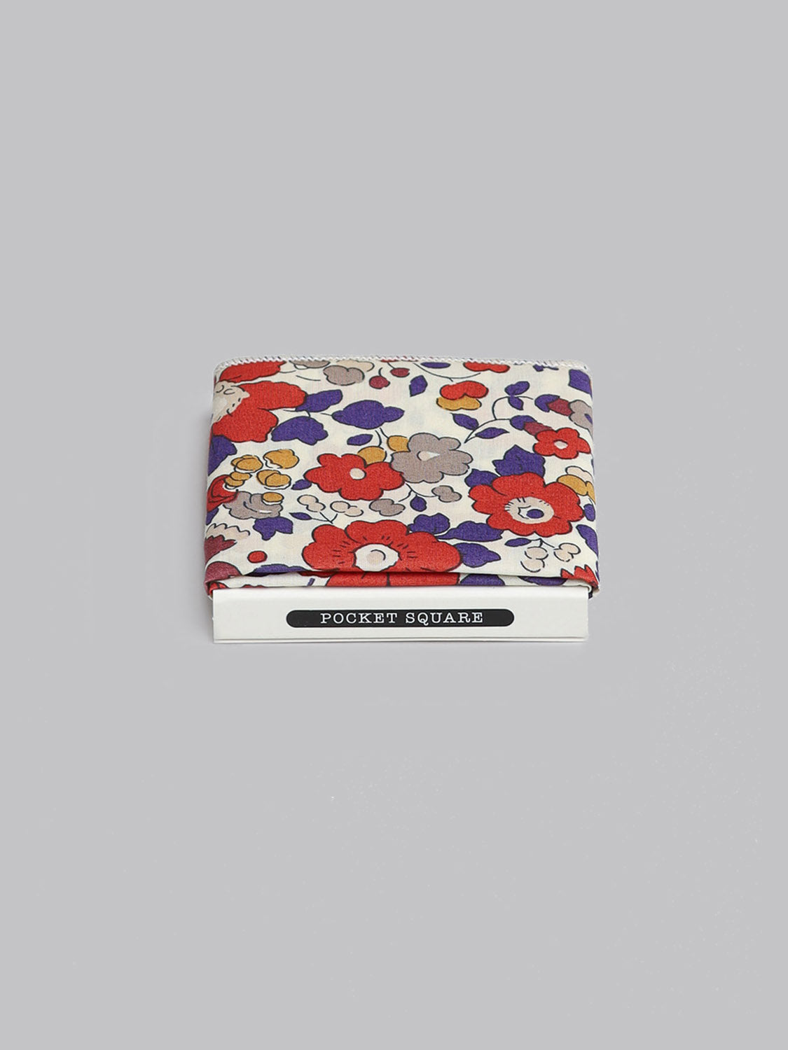 The Liberty™ Betsy Pocket Square by ID Menswear features a red, purple, yellow, and gray floral print on luxurious Tana Lawn cotton. It is shown folded on a light gray background with a POCKET SQUARE label.