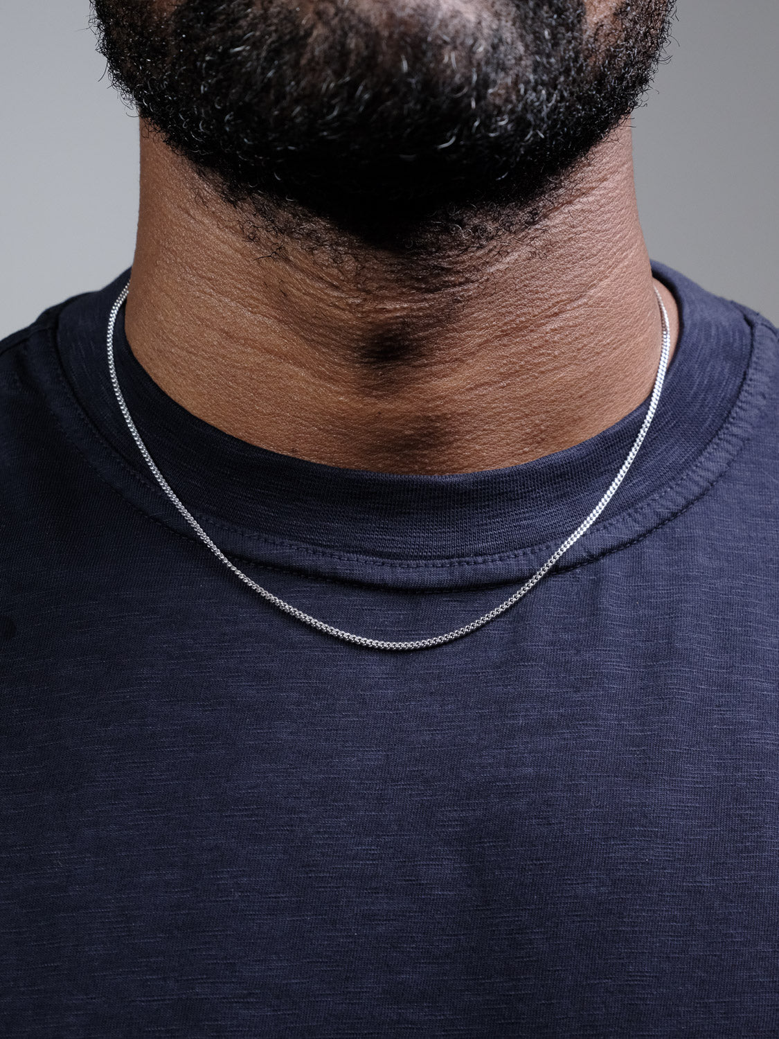 Close-up of a person wearing a dark navy blue shirt and the Blaze 60 Miami Cuban Necklace by ID Menswear, with only the lower half of their face and neck visible.