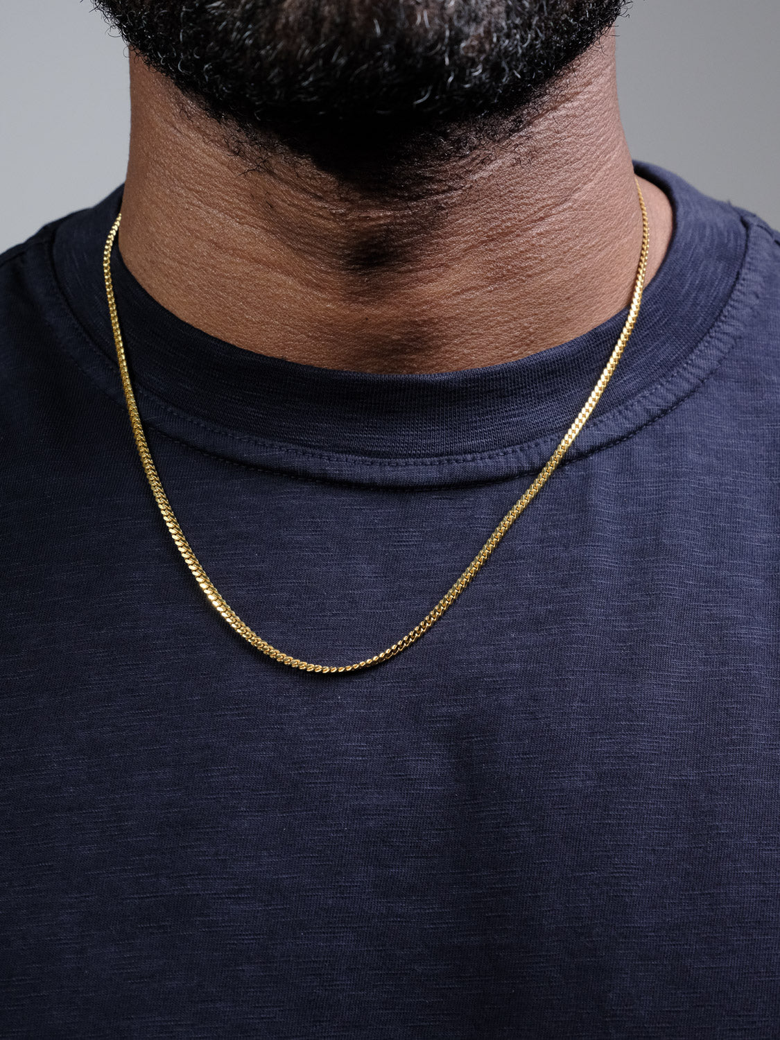 A close-up of a person wearing a dark blue shirt and the ID Menswear Blaze 100 Miami Cuban Necklace, with only the lower half of their face and neck visible.